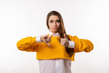 Portrait of attractive brunette girl showing thumb up and thumbs down, difficult choose. Human emotions, gesture concept