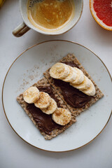 a cup of coffee with milk and crispbreads with chocolate paste and banana pieces