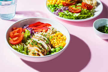 Grilled chicken breast with brown rice and vegetables in white plate, pink background. Healthy food concept.