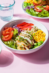 Grilled chicken breast with brown rice and vegetables in white plate, pink background. Healthy food concept.
