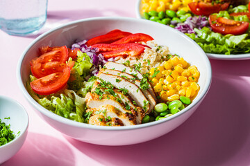 Grilled chicken breast with brown rice and vegetables in white plate, pink background. Healthy food concept.