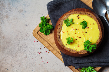 Cheese soup in a bread bowl on wooden board. Czech cuisine concept.
