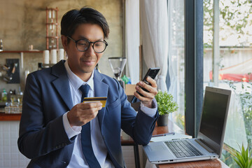 Front Right Smile Asian Businessman in Suit Wear Glasses Using Smartphone for Online Shopping in Coffee Shop Scene. Asian Businessman Work from Anywhere with Technology