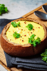 Cheese soup in a bread bowl on wooden board. Czech cuisine concept.