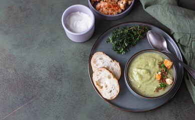 Broccoli cream soup decorated with thyme, cream, roasted cauliflower and fresh bread on green concrete background. Healthy vegetarian food concept. Top view.