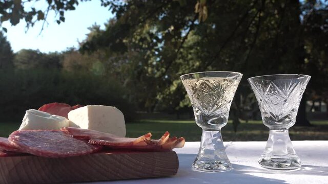 Pouring Homemade Balkan Rakija Brandy in Small Glasses on PIcnic Table