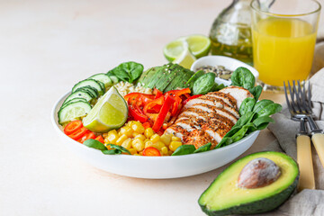 Healthy buddha bowl lunch with grilled chicken and bulgur, spinach, avocado, cucumber, bell pepper and corn on light background. Delicious balanced food concept.