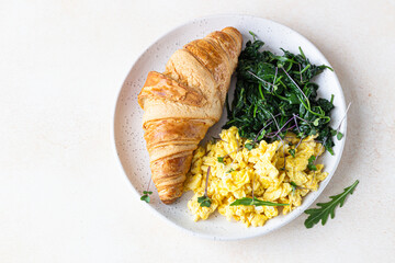 Croissant served with scrambled eggs and spinach on plate, light concrete background. Breakfast. Top view.