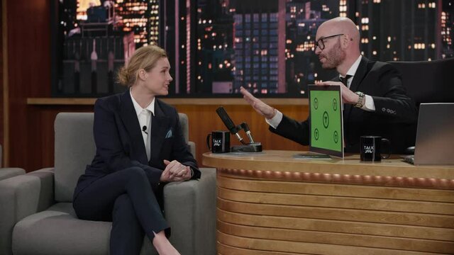 FIXED Late-night talk show host showing a green board with tracking points to female celebrity polititian guest in a studio. TV broadcast style show. Shot with RED cinema camera