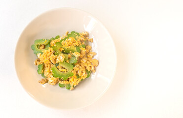 Stir-fried bitter gourd with egg in round dish. Flat lay healthy food on warm light background. Top view food image Asia dish stir-fried bitter gourd with egg.