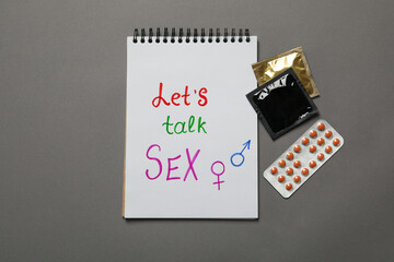 Notebook with Let's talk Sex, condoms and pills on gray background
