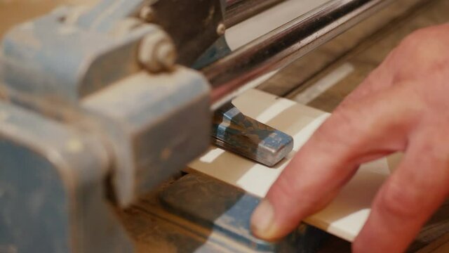 Close up of tiler with a hand-held tile cutter cuts the tile on the floor, person cutting ceramic tiles