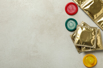 Multicolored condoms on white textured background, space for text