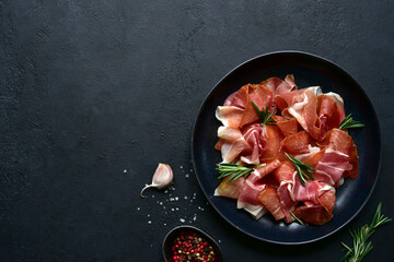 Slices of prosciutto di parma or jamon serrano (iberico)  on a black plate. Top view with copy space. - obrazy, fototapety, plakaty