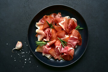 Slices of prosciutto di parma or jamon serrano (iberico)  on a black plate. Top view with copy space. - obrazy, fototapety, plakaty