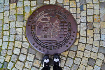 Hatchway on the cobblestone street and shoes on it. Bergen, Norway