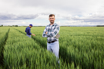 Portrait of farmer standing in green wheat field with his colleague in background. © Zoran Zeremski
