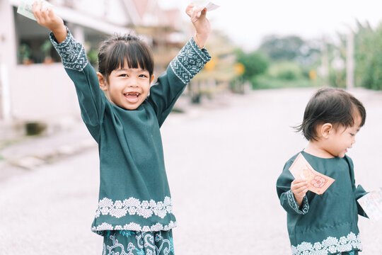Cute Malay girls siblings sisters in Malay traditional cloth showing his happy reaction after received money pocket during Eid Fitri or Hari Raya celebration