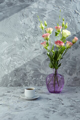 Wonderful breakfast. A bouquet of pink eustoma flowers on a gray background. A Cup of black coffee is nearby