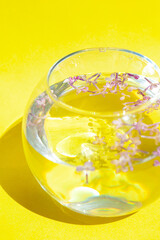 Lilac flowers float in the water. Purple and pink flowers in a glass vase. On a yellow  background