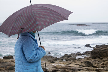 woman in coat and umbrella in front of the coast