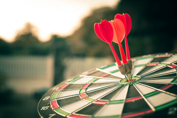 Fototapeta premium Close up shot of the dart arrow hit on bulleyes of dartboard to represent that the business reached the target with dark tone picture style. Target and goal as concept.