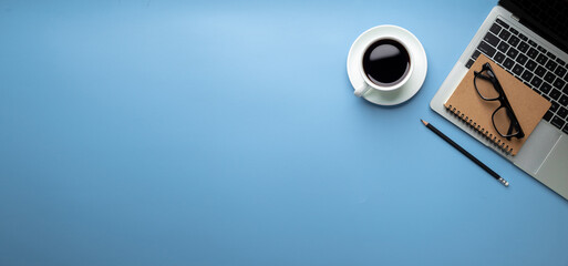 Flat lay, top view office table desk. Workspace with, laptop,office supplies, pencil, green leaf, and coffee cup on blue background.