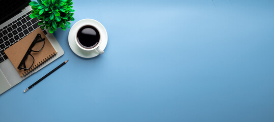 Flat lay, top view office table desk. Workspace with, laptop,office supplies, pencil, green leaf, and coffee cup on blue background.