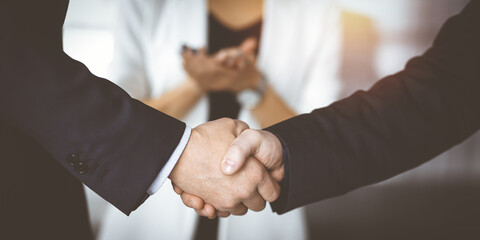 Obraz premium Unknown businesspeople are shaking their hands after signing a contract, while standing together in a sunny modern office, close-up. Business communication, handshake, and marketing concept