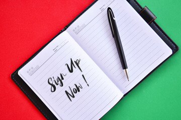 'Sign up now!' word on notebook with red and green background flat lay concept.