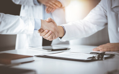 Unknown doctors are shaking their hands as agreement about patient's diagnosis in a sunny cabinet, close-up. Perfect medical help, insurance in health care, medicine concept