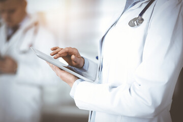 Unknown woman doctor is checking some data at computer tablet, close up. Young doctors at work in a sunny hospital. Perfect medicine concept