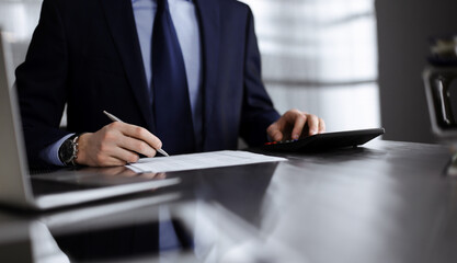 Unknown man accountant in blue blazer use calculator and computer with holding pen on while staying at home during covid pandemic. Taxes and audit concept
