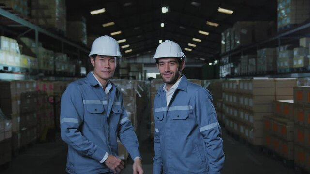 portrait of asian male and caucasian male professional enginner wearing uniform hardhat standing and smile with confident and cheerful in warehouse factory