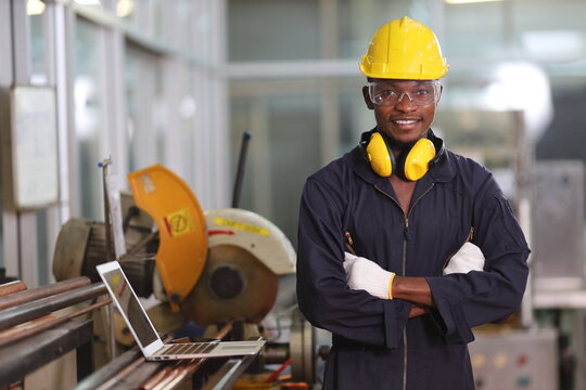 Portrait of African American mechanic engineer worker wearing safety equipment beside the sawing machine in manufacturing factory