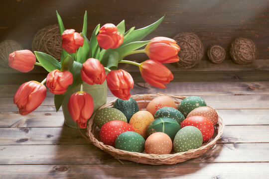 Bunch of red tulips, Easter eggs in wattle tray. Springtime decorations on rustic wooden background. Retro toned image of Easter decorations.in low key. Sunlight with shadows.