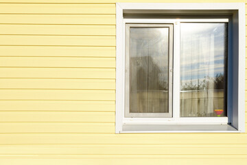 white plastic window on the wall lined with yellow siding