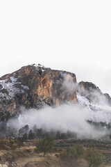Snowy rocky mountain with foggy clouds in winter
