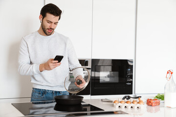 Happy man taking photo on cellphone while cooking scrambled eggs