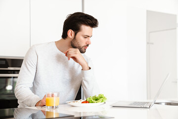 Fototapeta na wymiar Focused handsome man using laptop while having breakfast