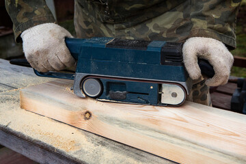 Hands of a joiner with a grinder machine. Flying shavings, wooden board. The work of a professional. Woodwork.