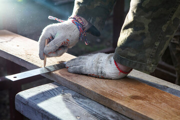 Carpenter's hands. The carpenter makes marks on the board with a pencil and ruler. The work of a professional. Woodwork.