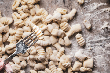 floured fork holding a gnocchi, background with many gnocchi, homemade food