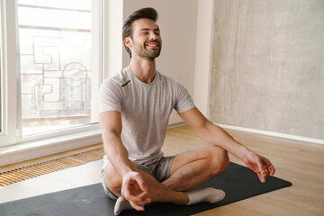 Happy athletic handsome man meditating after workout at home - obrazy, fototapety, plakaty