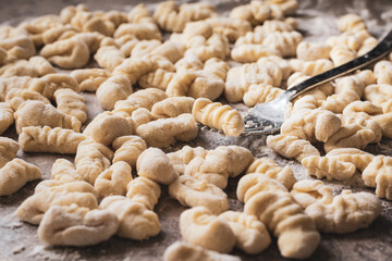 floured fork holding a gnocchi, background with many gnocchi, homemade food