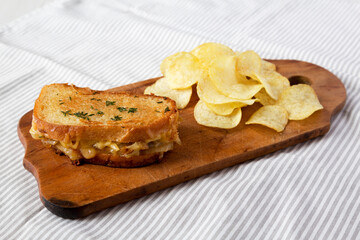 Homemade French Onion Melt Cheese Sandwich with Chips on a rustic wooden board on cloth, side view.