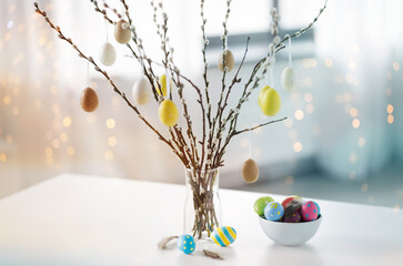 holidays and object concept - pussy willow branches decorated by easter eggs in vase on table over...