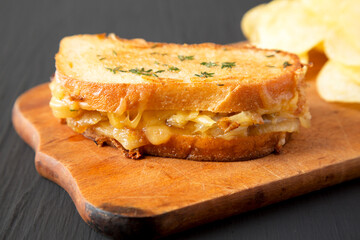 Homemade French Onion Melt Cheese Sandwich with Chips on a rustic wooden board on a black surface, low angle view. Close-up.