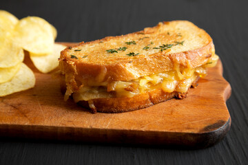 Homemade French Onion Melt Cheese Sandwich with Chips on a rustic wooden board on a black background, low angle view. Close-up.
