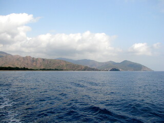 Panorama of the blue sea surface on the background of mountain ranges illuminated by the morning sun on the horizon.